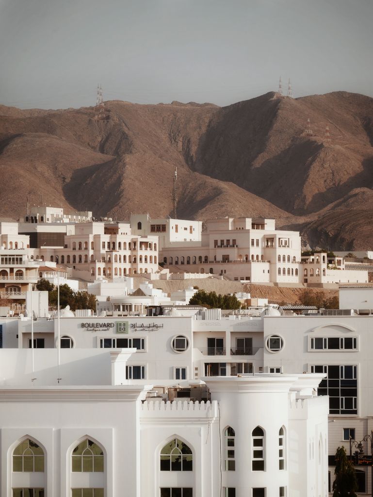 Scenic view of Muscat's traditional architecture against rugged mountains during the day.