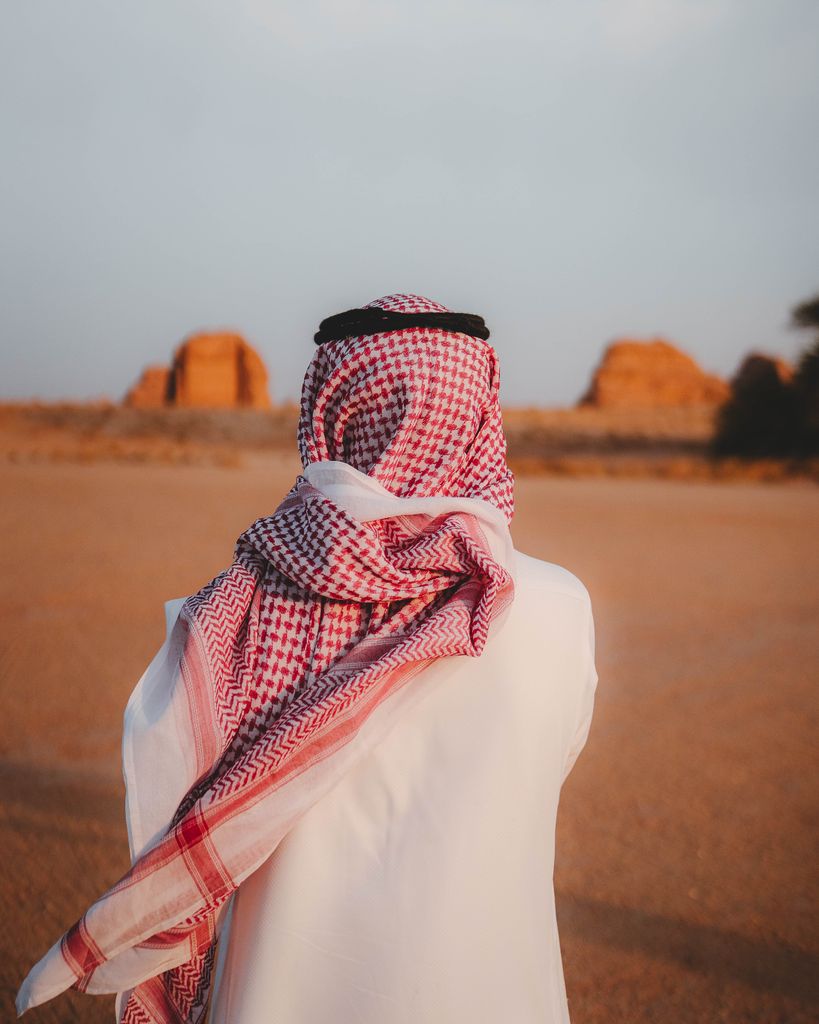 A person in Middle Eastern attire stands in a serene desert landscape at sunset.